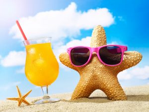 Starfish, sunglasses and cocktail on sand with sky in the background